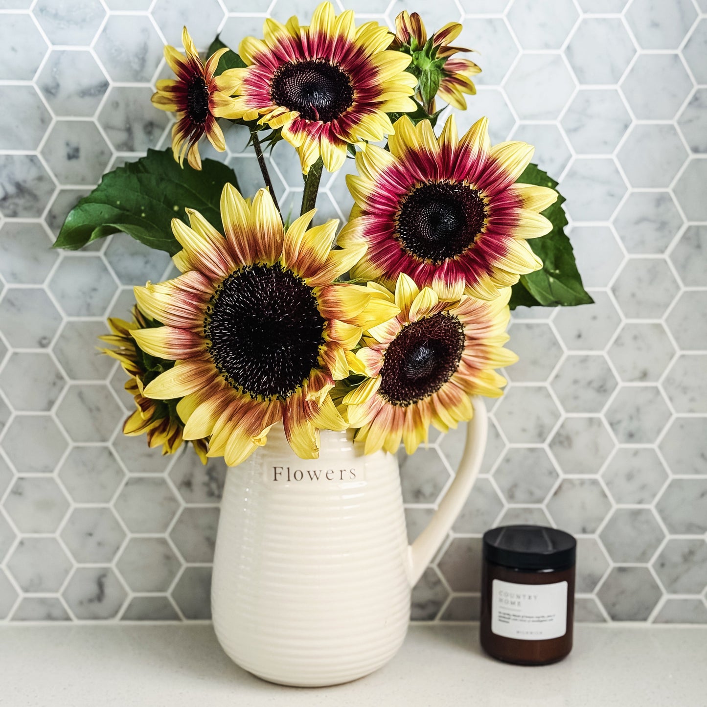 Sunflower arrangement in a white vase on a marble countertop with a hexagonal tile pattern.