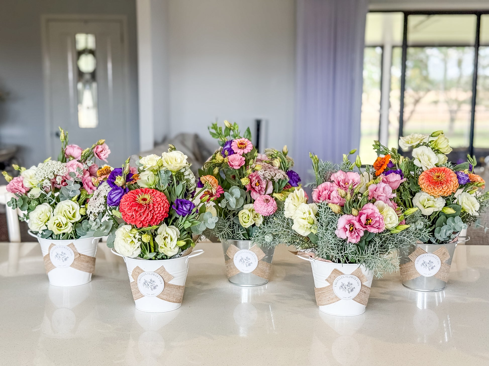 Five colourful flower bouquets in decorative pots on a table.