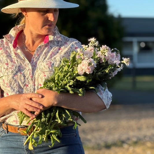 Person holding a bundle of greens and a bouquet of flowers outdoors